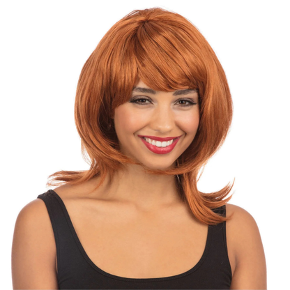 A woman wearing a short, layered wig with straight bangs in a warm coppery orange-red shade, paired with a black tank top, against a plain white background.