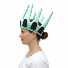 A woman in profile wearing a mint green and black crown inspired by the Statue of Liberty, shown against a plain white background.