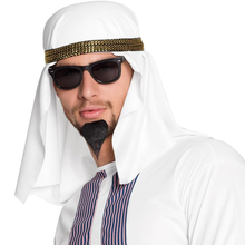 A man wearing a white traditional thobe and keffiyeh headwrap with a metallic gold headband, black sunglasses, and a black goatee, shown against a plain white background.