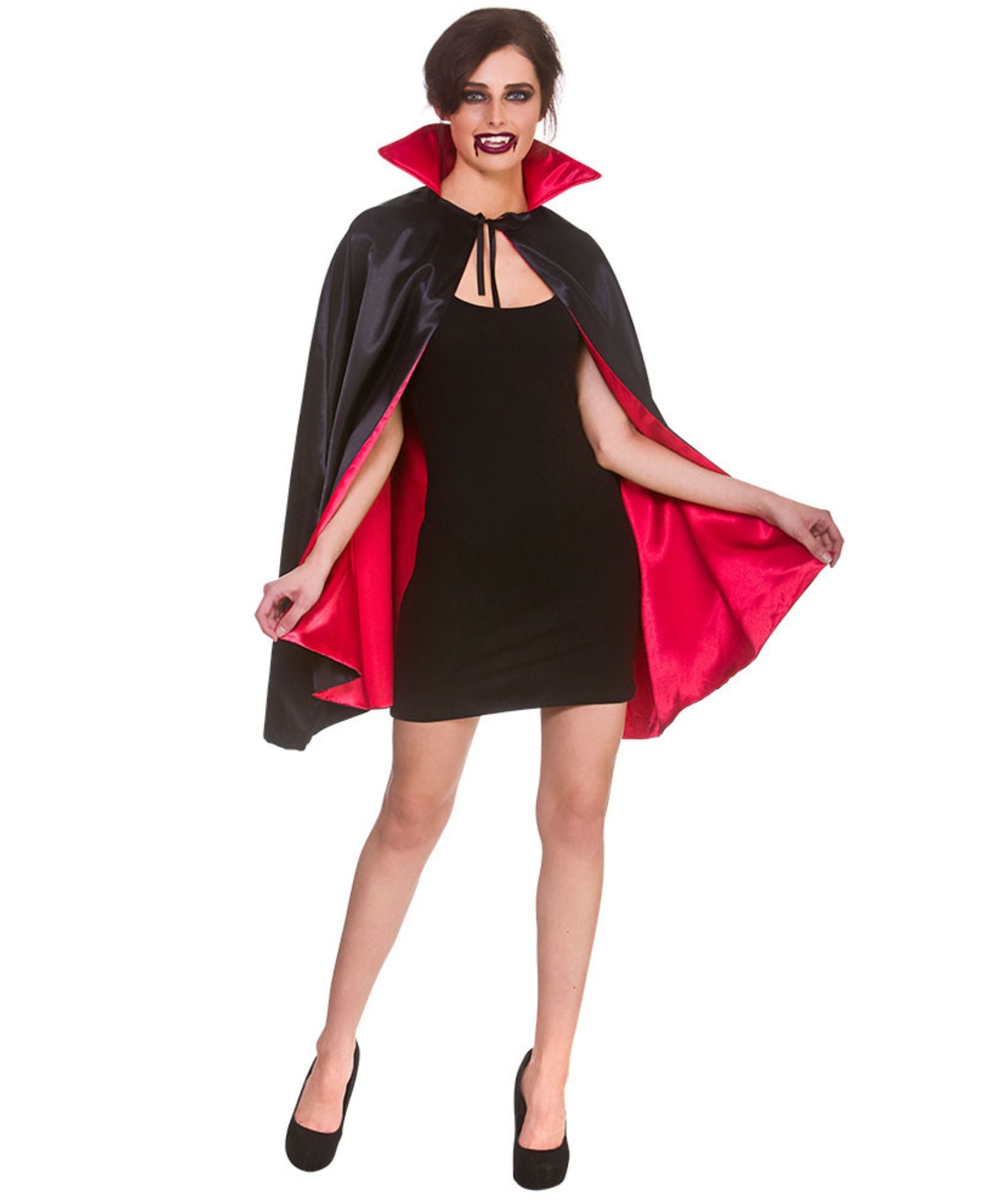 A woman modeling a vampire costume consisting of a black satin cape with a bright red inner lining, worn over a black mini dress and black heels, against a plain white background.