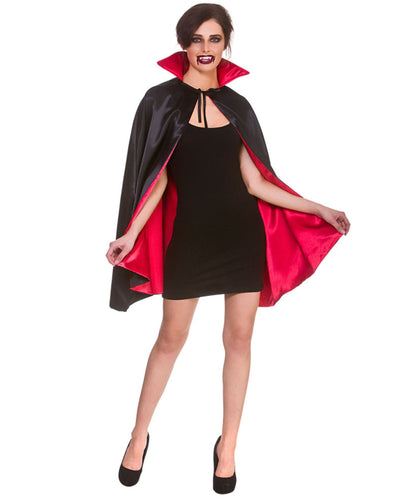 A woman modeling a vampire costume consisting of a black satin cape with a bright red inner lining, worn over a black mini dress and black heels, against a plain white background.