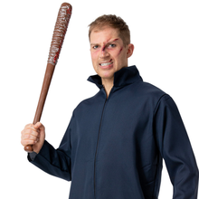 A man wearing a dark navy blue zip-up jacket and holding a brown toy baseball bat with a bloody bat handle, posed against a solid white background.
