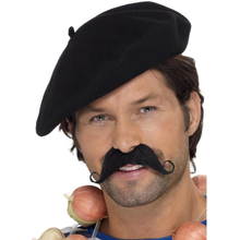 A man wearing a black felt beret and a black curled mustache, with onions held near his neck, against a plain white background.