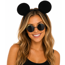 A woman with long wavy blonde hair wearing a black mouse ears headband and round black sunglasses, shown against a plain white background.