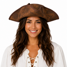 A smiling woman with long wavy brown hair wearing a brown distressed pirate tricorn hat and a white lace-up blouse, photographed against a solid white background.