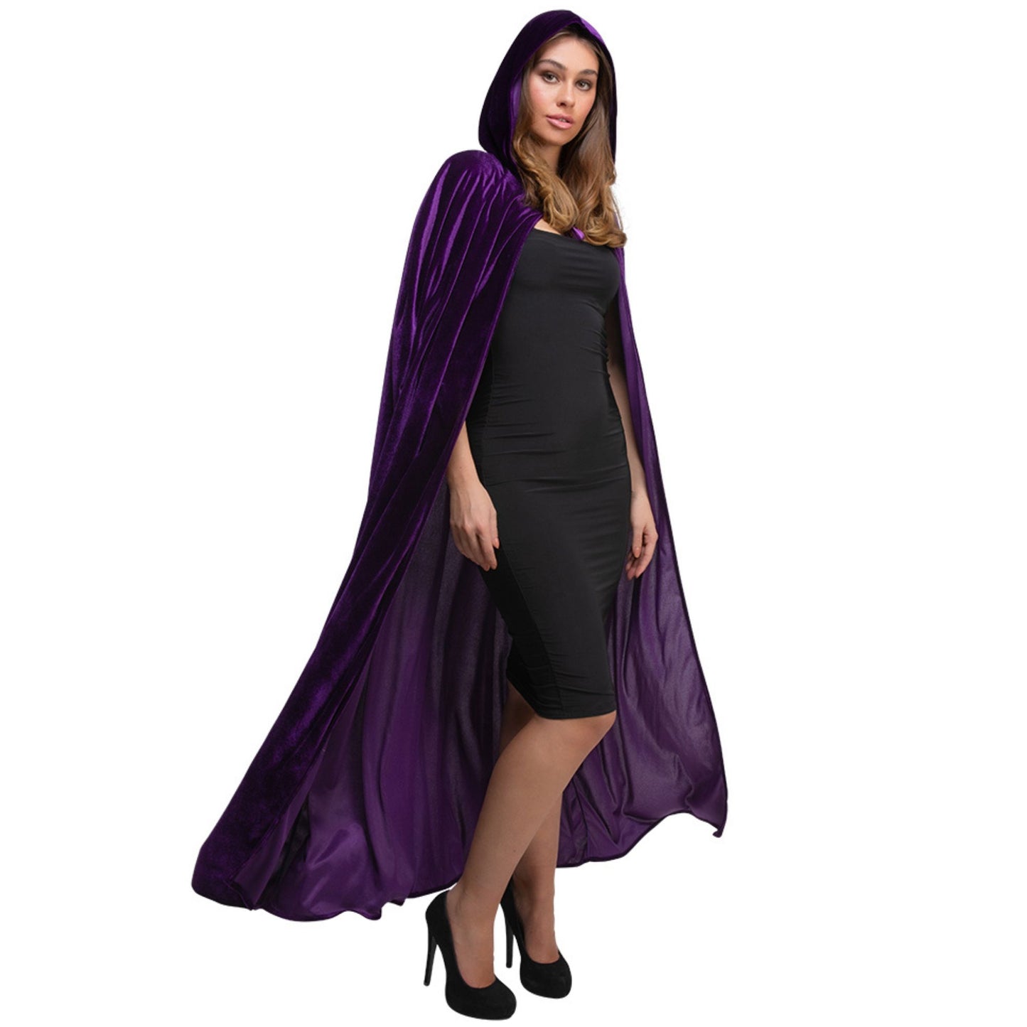 A woman modeling a long, flowing purple velvet cape with a hood over a black dress and black heels, set against a plain white background.