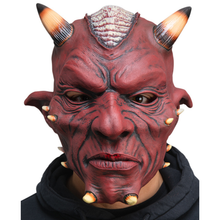 A red devil mask with horns, black textured markings, and a black hoodie worn by a person against a white background.