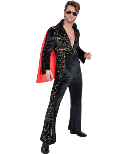 A man modeling a black velvet Elvis-style costume jumpsuit with gold sequin embellishments, a red cape, and gold sunglasses against a plain white background.