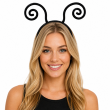 A smiling blonde woman wearing a black headband with two spiral antennae, photographed against a plain white background.