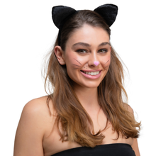 A woman with brown hair wearing a black cat ears headband and cat face makeup, including a pink nose and whiskers, against a plain white background.