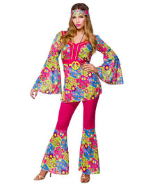 A woman modeling a colorful 1960s-style hippie costume set featuring a long-sleeve bell-sleeve top with a floral and psychedelic pattern, matching flare pants, a matching headband, and a pink waist belt with a peace sign medallion.