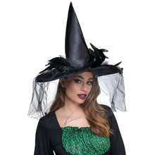 Woman wearing a black witch hat with feathers and a veil on a white background